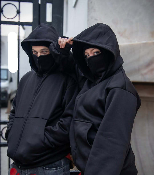 Two people wearing black hoodies and face coverings in front of a 'Fast Shop' sign.